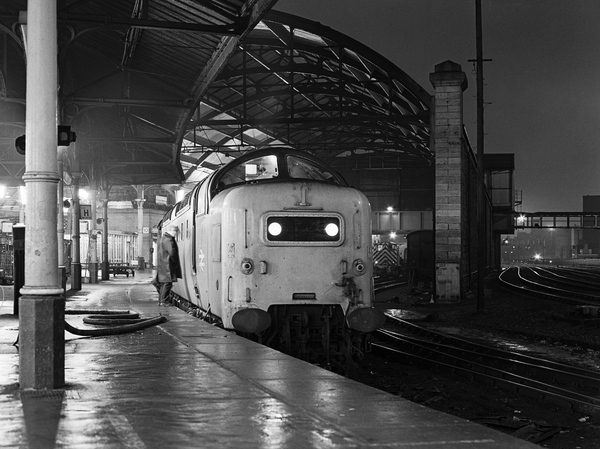 Black-and-white night photograph of Deltic 55008 The Green Howards at Newcastle Central with the Up Night Aberdonian, beside a wet platform beneath the canopy